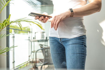 The woman uses a mobile phone. casual style. A middle-aged woman looks at her phone, close-upの写真素材