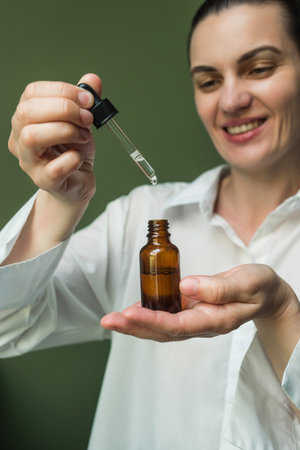 A smiling woman in a white shirt holds a bottle of essential oil in her hands and drips it from a...