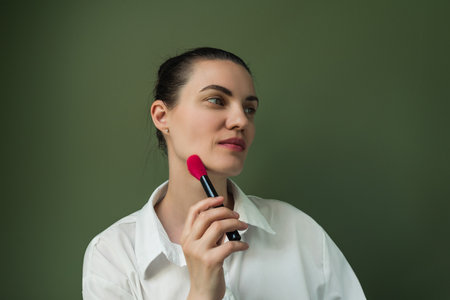 Makeup artist powder and brush. Beautiful woman face. Woman puts blush on cheeks. make up in process. European woman uses makeup brushの写真素材