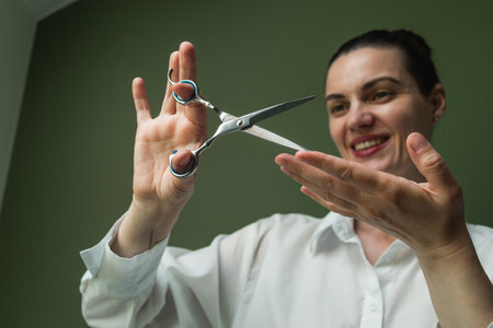 Photo of a hairdresser, a master, with professional scissors in her hands, wearing a white shirt against an isolated green backgroundの写真素材