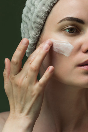 An attractive European woman puts cream on her face. Close-up of the beauty industry, cosmetology. skincare at homeの写真素材