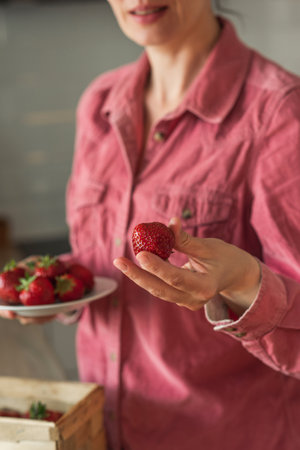 A sweet smiling mature woman holds out a strawberry. Strawberry in the hands of a womanの写真素材