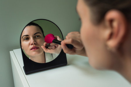 A European woman applies makeup in front of a mirror. Make-up in front of the mirror. The reflection of a woman in the mirror. beauty and self-careの写真素材