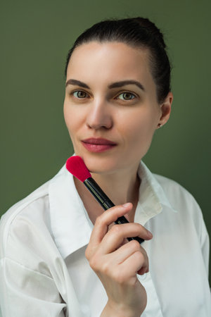 Makeup artist powder and brush. Beautiful woman face. Woman puts blush on cheeks. make up in process. European woman uses makeup brushの写真素材