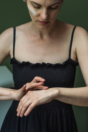 A woman in a black dress puts cream on her hands. Moisturizing the skin of the hands, cosmetology,...