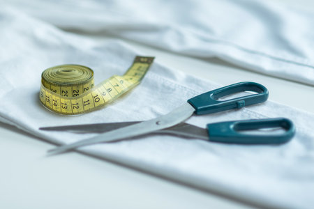 Shortening jeans. White jeans, Measuring tape, scissors on table. Jeans cutting. Making shorts at homeの写真素材