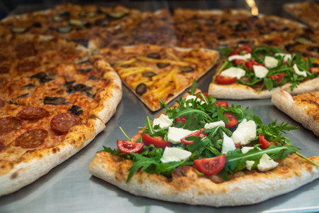 Close-up of a slice of pizza in a cafe. Sale of ready-made pizza in a pizzeria. Italian pizza with arugulaの写真素材