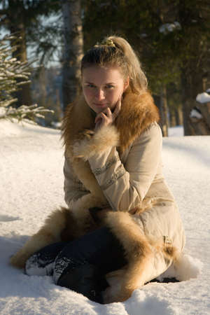 Young beautiful girl sitting on snow in wood.の写真素材