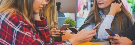 Group of people sitting around the table while holding smartphones - Teenagers obsessed with technology and using cellphones in bar hangging with each other- Youth lifestyle conceptの写真素材