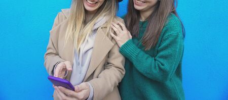 Teenagers with smartphone navigating online by a wall background - Girls looking at each others...