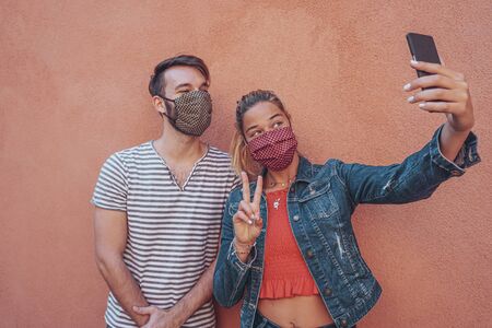 Friends takeing a selfie with face mask on in coronavirus time for protection - Young people using technology outdoorsの写真素材