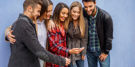 Group of people standing by the wall and sharing online stuff- Friends checking out their smartphones- Technology conceptの写真素材