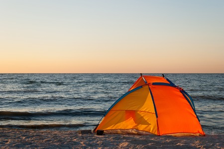 bright orange yellow tent empty, sunrise on the seashore, in the sun, against the blue sea and blue sky, yellow sand, beach, rest, summerの写真素材