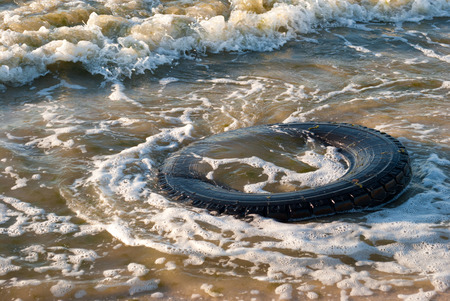 Large-scale rubber tire on the ocean shore, summer sunny day beach