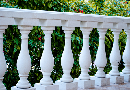 White marble columns in a row, parapet, fence, against the background of green flowering bushes, flowers, in the shade, architecture, olden time, fence, vintage, artの写真素材