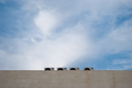 Four outdoor air conditioning units on a marble wall, against a background of blue sky and white clouds, cloudy day, architectureの写真素材