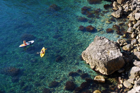 Two tourists on a kayak pass by a steep rocky shore of the sea in the Crimea. Beautiful sports holidaysの写真素材