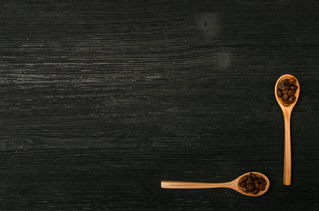 Coffee beans in wooden spoons and coffee scattered on a black table surface background with copy space. Top view.の写真素材