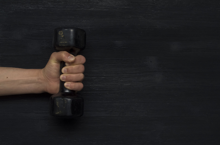 Male hand holds a dumbbell on a black black background. Abstract gym sport background.の写真素材