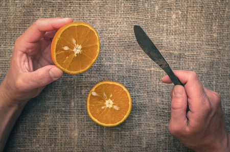 Cut orange in the man hands on the burlap sackcloth table background. First-person photo.の写真素材