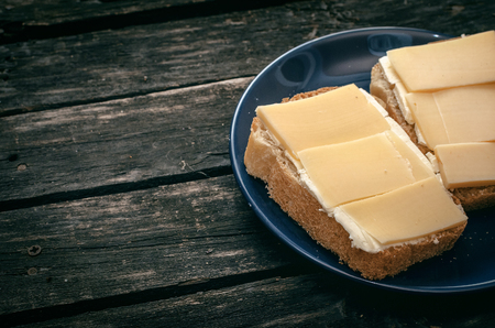 Sandwich with cheese and butter on the blue plate. Rustic kitchen. Simple breakfast. Fast food.の写真素材