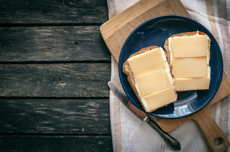 Sandwich with cheese and butter on the blue plate. Rustic kitchen. Simple breakfast. Fast food.の写真素材