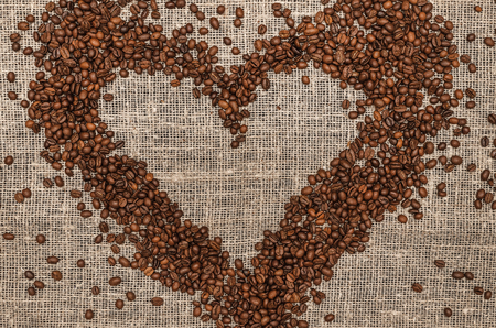 Coffee beans made in the heart shape form on burlap cloth background with copy space in the center.の写真素材