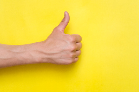 Male hand showing a thumbs up gesture isolated on yellow background.の販売画像