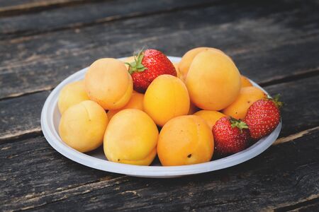 Apricot and strawberry in plate on the old wooden table.