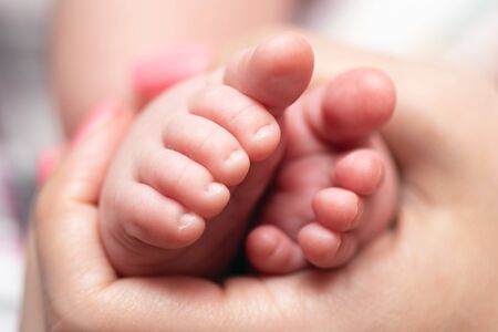 Young mother is holding in hands a small feet of her baby.の写真素材