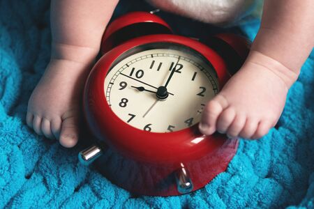 Baby feet and a red alarm clock on a blue towel background.の写真素材