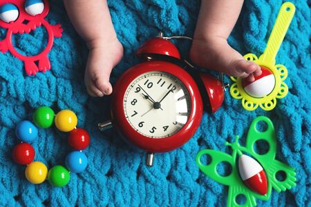 Baby feet and a red alarm clock and child toys on a blue towel background.の写真素材