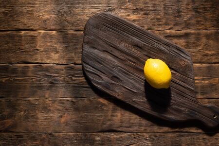 Old cutting board with a copy space for food and with a yellow limon above on a aged wooden kitchen board background.の写真素材