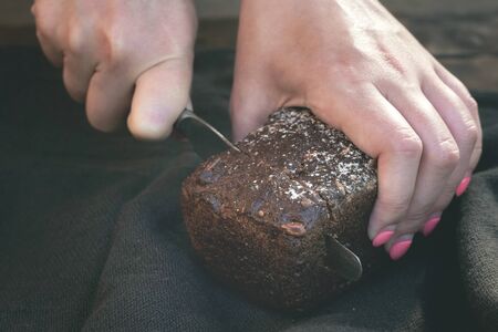 Woman is cutting a fresh bread by a kitchen knife on a cutting board.