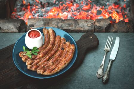 A grilled sausages on a plate on a kitchen table with a burning coals background.の写真素材