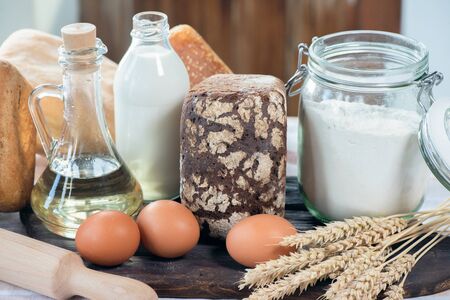 Bread, bottle of sunflower oil, jar with flour, milk and wheat stems on the rustic kitchen table...