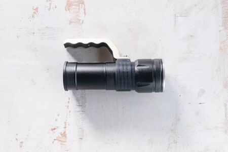 Modern black flashlight with handle on the old white wooden table background.