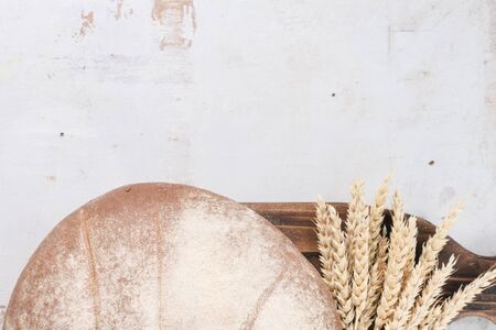 Fresh bread and wheat stems on the cutting board on the rustic white table flat lay background with...
