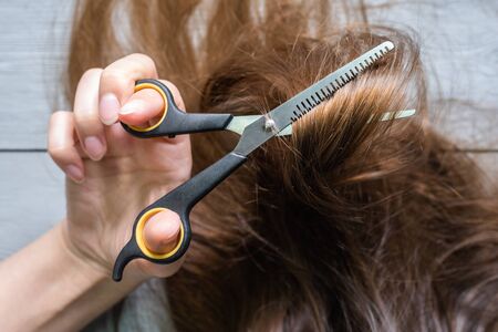 Woman cuts her hair by a scissors close up.の写真素材