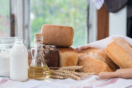 Various kinds of bread, bottle of sunflower oil, jar with flour, milk and wheat stems on the rustic...