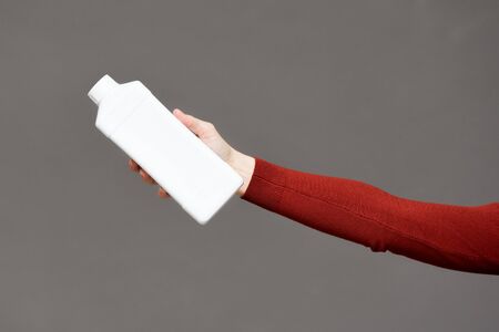 White detergent bottle in female hand on gray background.
