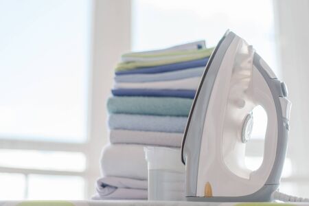 Electrical iron and clean clothes on a ironing board background.の写真素材
