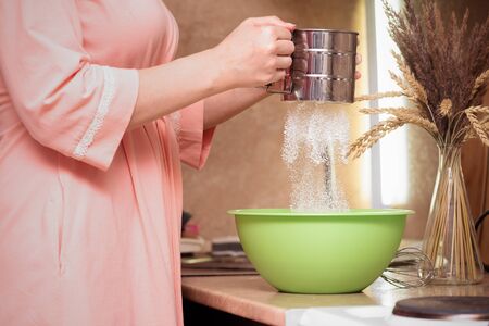 Woman is sifting flour for dough through the sieve.