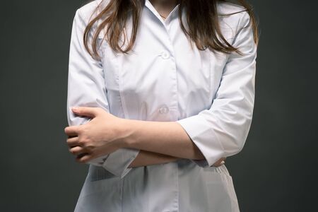 Doctor in medical gown is standing with crossed arms close up on dark background.の写真素材