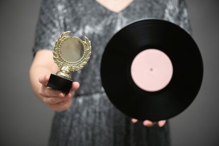 Music award ceremony concept. A singer with golden award trophy and vinyl record in hands on gray background.の写真素材