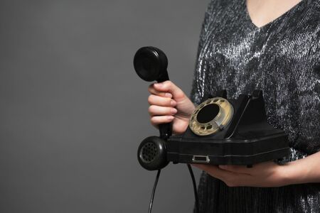 Old black rotary phone in woman hands close up on gray background with copy space. Contact us.