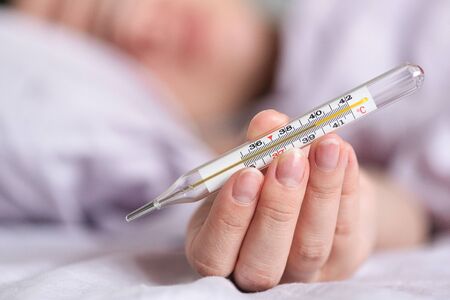 Thermometer in hand of flu sick woman in a bed.
