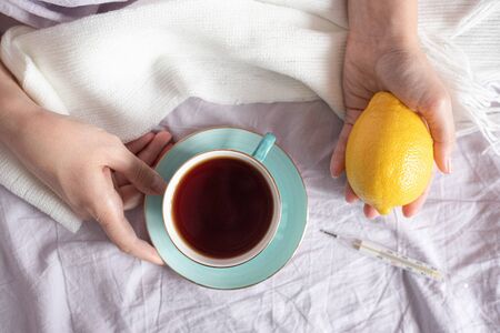 Flu sick woman in a bed with a cup of tea and fresh lemon.