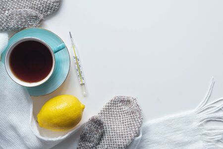Cup of hot tea, lemon, thermometer and scarf on white table flat lay background.