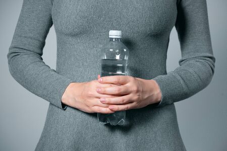 Bottle of water in female hands closeup on gray background.の写真素材